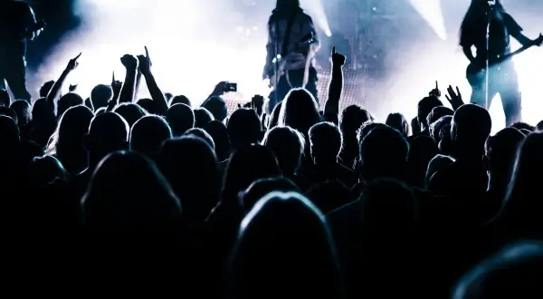 Tłum ludzi na koncercie, z rękami w górze, wpatrujący się w scenę z muzykami.