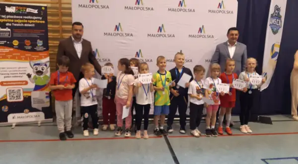 Dzieci z dyplomami i medalami stoją przed banerem "Małopolska".