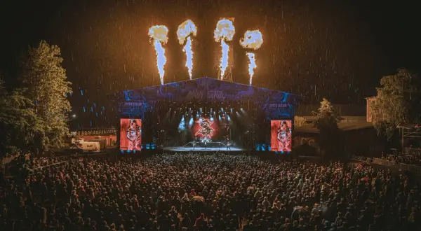 Koncert na Mystic Festival w deszczu, z płomieniami nad sceną i tłumem fanów.
