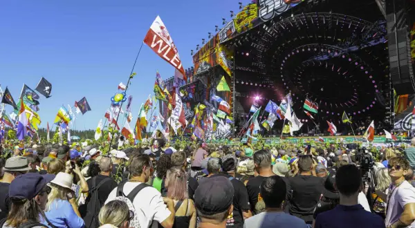 Tłum ludzi na festiwalu muzycznym z flagami i sceną w tle.
