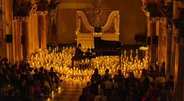 Pianista gra na fortepianie otoczony tysiącami świec, przed publicznością.