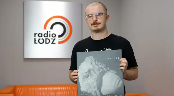 Mężczyzna w okularach trzyma płytę winylową The Cure "Songs of a Lost World" na tle logo Radia Łódź.