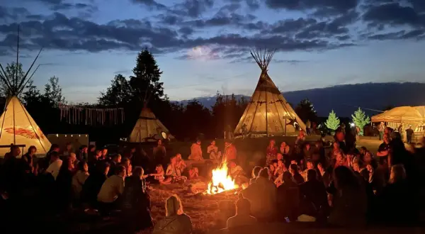 Ludzie siedzą przy ognisku pod namiotami tipi, tworząc atmosferę jednego z wielu festiwali na świecie.