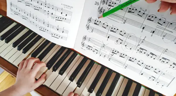 Dziecko uczy się gry na keyboardzie, ćwicząc nuty z podręcznika. Zielony ołówek zaznacza fragment do nauki.