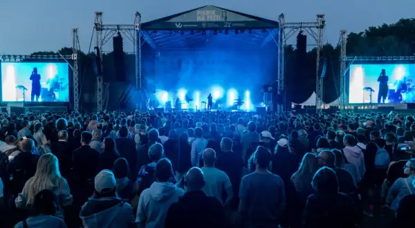 Koncert na festiwalu w Cytadeli, tłum ludzi przed sceną oświetloną niebieskim światłem.