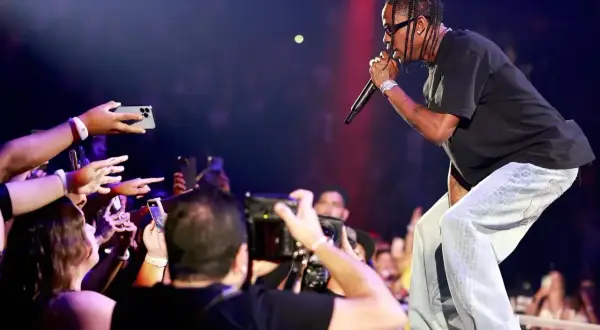 Travis Scott koncert: artysta śpiewa do mikrofonu, a fani z telefonami w dłoniach nagrywają występ.