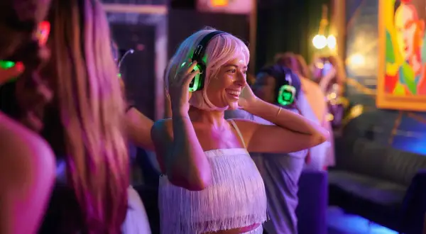 Kobieta w słuchawkach z podświetlanymi na zielono nausznikami tańczy na imprezie silent disco.