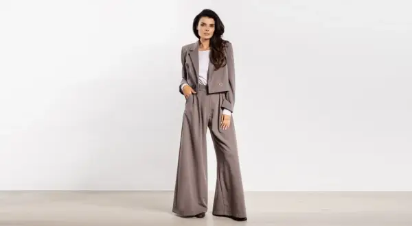 Kobieta w eleganckim, szarym garniturze z szerokimi spodniami i krótką marynarką.