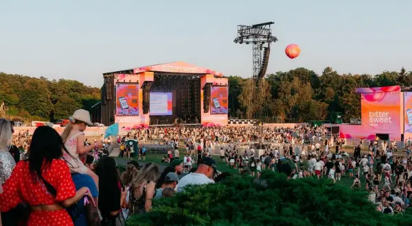 Tłum ludzi na festiwalu Bittersweet, scena w tle, różowe dekoracje i balon unoszący się na niebie.