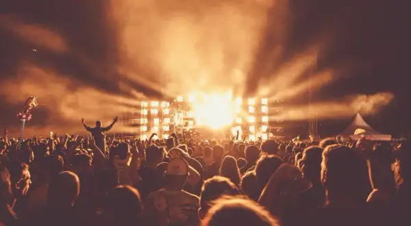 Tłum ludzi na festiwalu muzycznym, scena z jasnymi światłami i dymem.