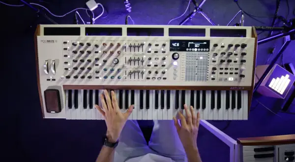 Dłonie grające na białym syntezatorze Arturia PolyBrute 12 z drewnianymi elementami.