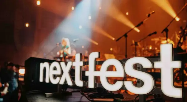 Światła sceny oświetlają napis "next fest" i artystkę grającą na gitarze.