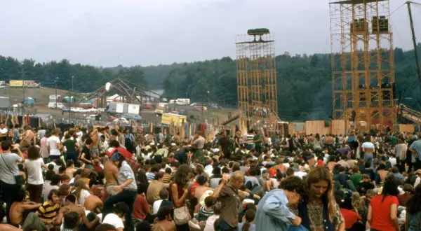 Tłum ludzi na festiwalu Woodstock, z widocznymi wieżami i sceną w tle.