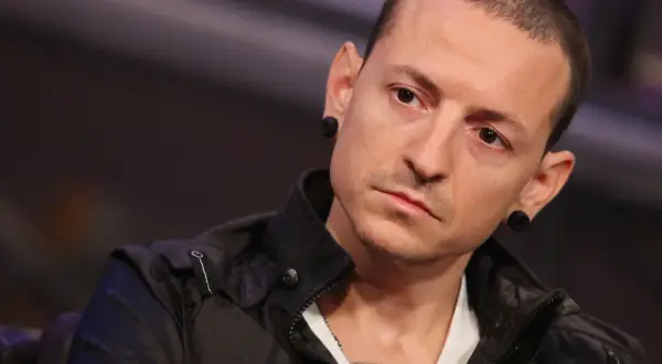 Chester Bennington z Linkin Park, z charakterystycznymi czarnymi tunelami w uszach, w czarnej kurtce.