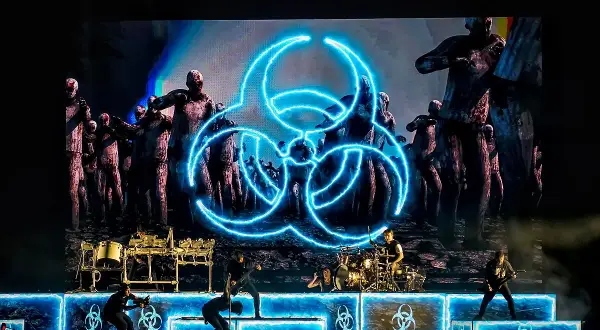 Koncertowy zespół na tle ekranu z symbolem biohazard i zombie.