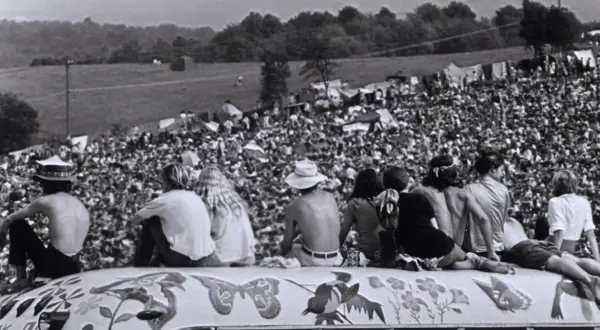 Widok z góry na tłum ludzi na festiwalu Woodstock '69, z kilkoma osobami siedzącymi na ozdobionej ciężarówce.