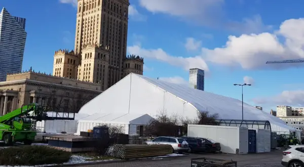 Biały namiot festiwalowy przed Pałacem Kultury w Warszawie, z nowoczesnymi wieżowcami w tle.
