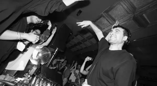 Energiczny DJ Fred Again w Polsce, tłum szaleje przy muzyce, dyskotekowa kula błyszczy.