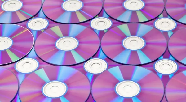Stos płyt CD/DVD z fioletowo-niebieskimi refleksami, widoczne środkowe otwory.