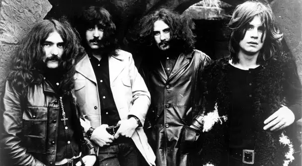 Czterech członków zespołu Black Sabbath pozuje do zdjęcia w mrocznym, kamiennym otoczeniu.