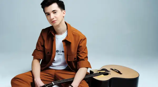 Marcin Patrzałek, młody muzyk, siedzi z gitarą, gotowy na koncert.