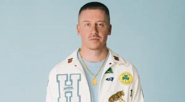 Macklemore w białej kurtce z naszywkami, gotowy na macklemore koncert polska.