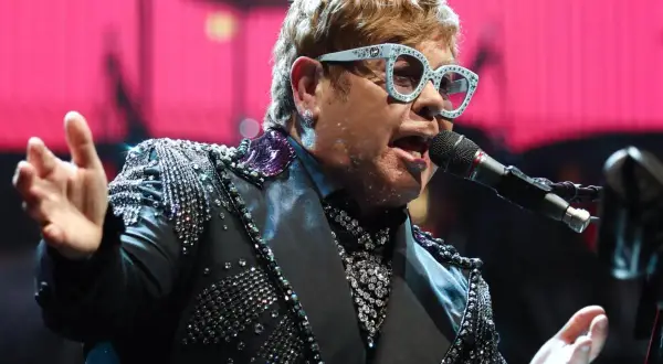 Elton John w błyszczącej marynarce śpiewa na jednym ze swoich niezapomnianych koncertów.