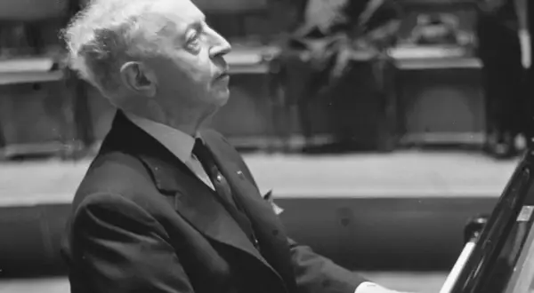 Artysta w garniturze, polski pianista jazzowy, pochyla się nad fortepianem, skupiony na grze.