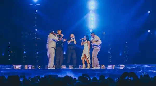 Zespół Pentatonix występuje na scenie w blasku niebieskich świateł, śpiewając do mikrofonów.