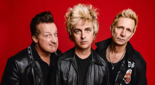 Trzech członków zespołu Green Day na czerwonym tle, w skórzanych kurtkach.