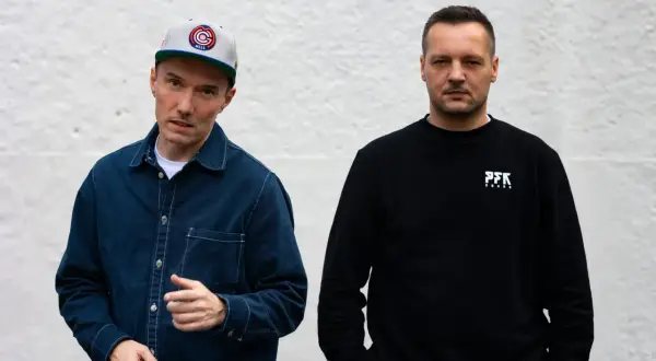 Dwóch członków Paktofoniki, jeden w czapce z daszkiem i granatowej kurtce, drugi w czarnej bluzie z logo PFK.