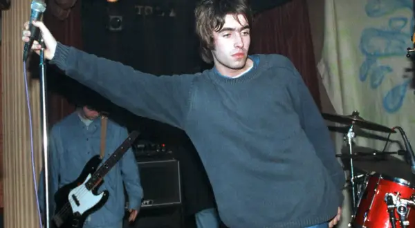 Liam Gallagher z Oasis śpiewa na scenie, w tle basista i perkusja. To klasyczne oasis utwory.
