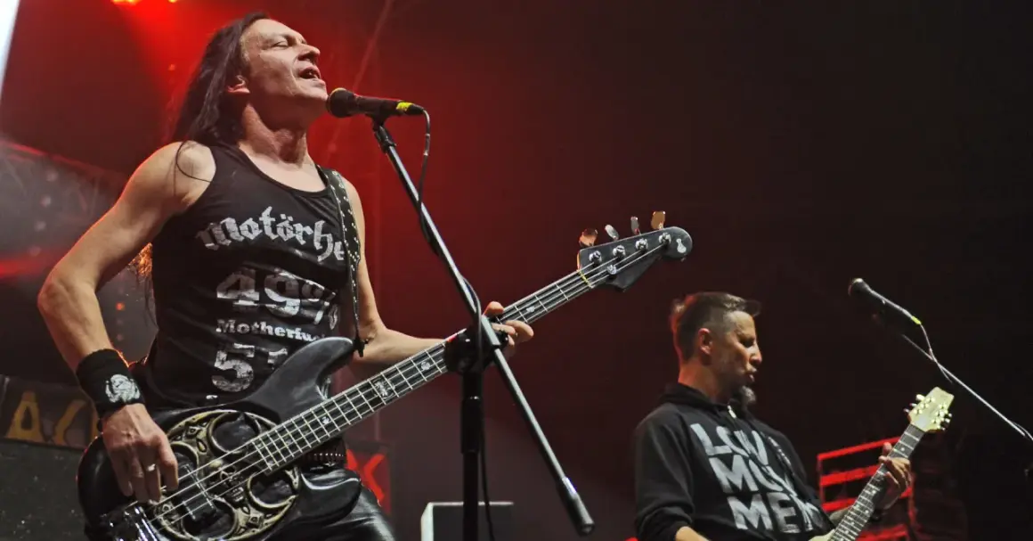 Dwóch muzyków Acid Drinkers grających na gitarach basowych na scenie.