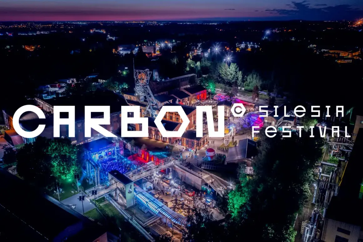 Nocne, oświetlone miasto i teren festiwalowy. Wielkie litery "CARBON Silesia Festival" na pierwszym planie.