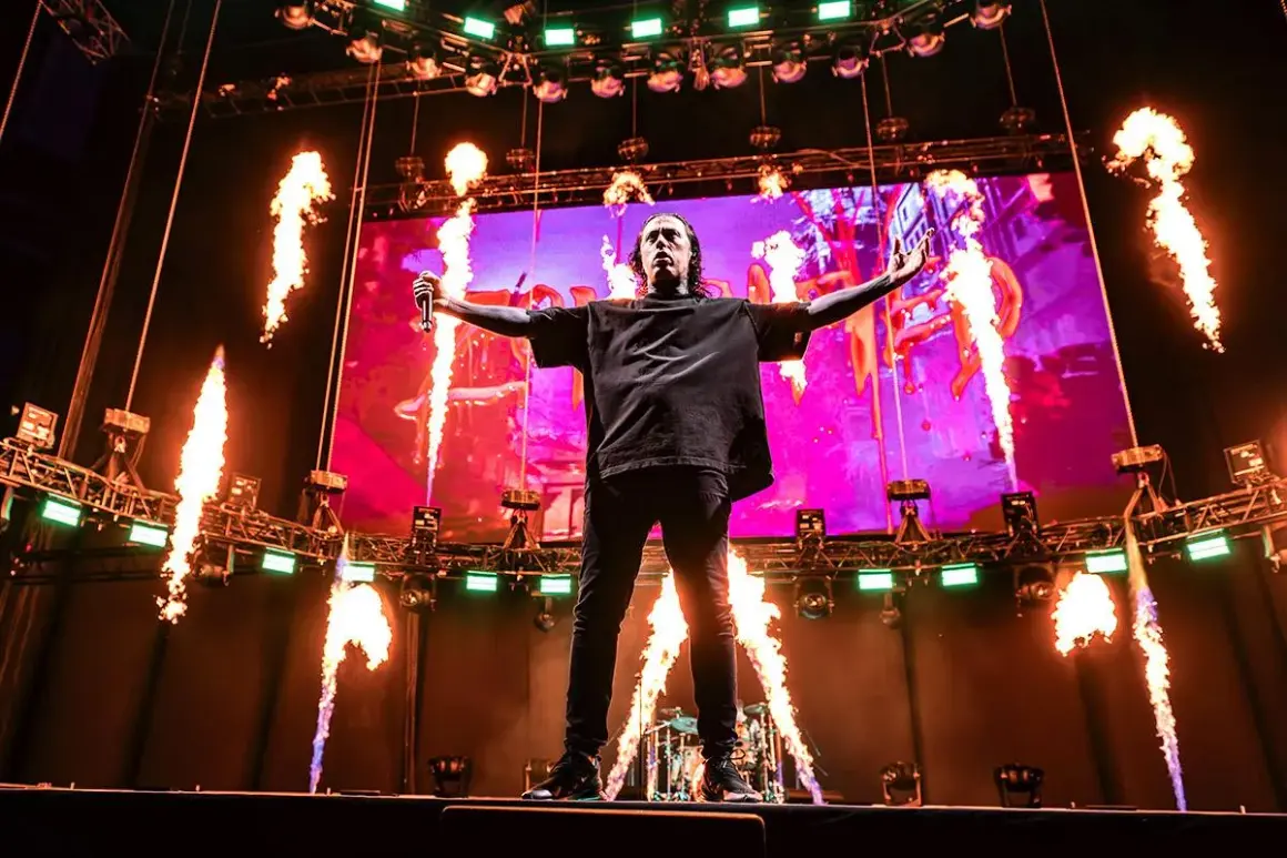Wokalista Falling in Reverse na scenie z płomieniami i ekranem w tle.
