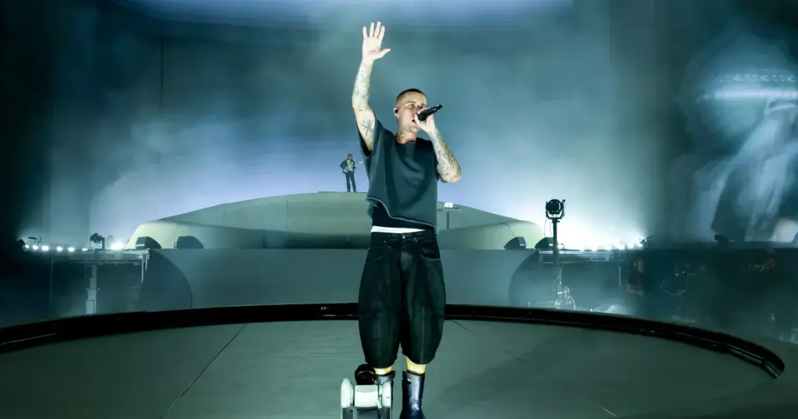 Justin Bieber śpiewa na scenie z podniesioną ręką, otoczony mgłą i światłami.