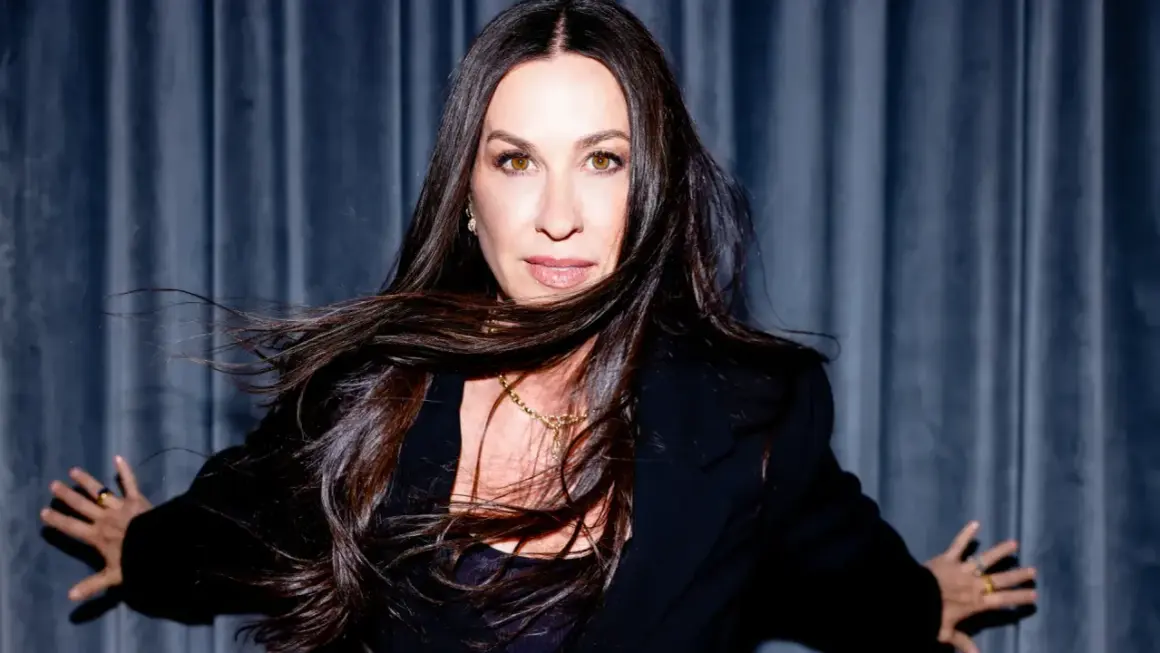Alanis Morissette z rozwianymi włosami, w czarnej marynarce, gotowa na koncert.