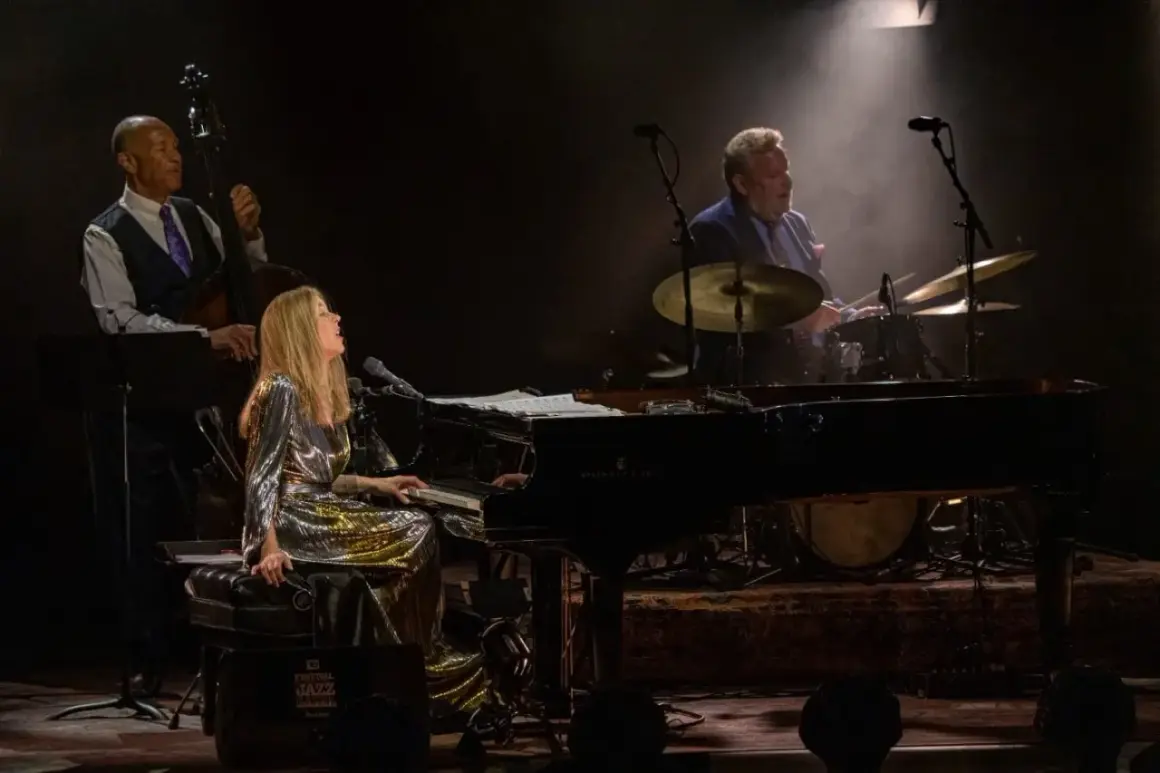 Diana Krall koncert: wokalistka i pianistka w błyszczącej sukni, kontrabasista i perkusista tworzą magiczną atmosferę jazzowego wieczoru.
