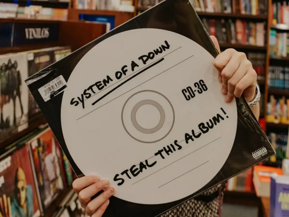 Ręce trzymają okładkę płyty System of a Down "Steal This Album!". Wybór między winylami a CD.