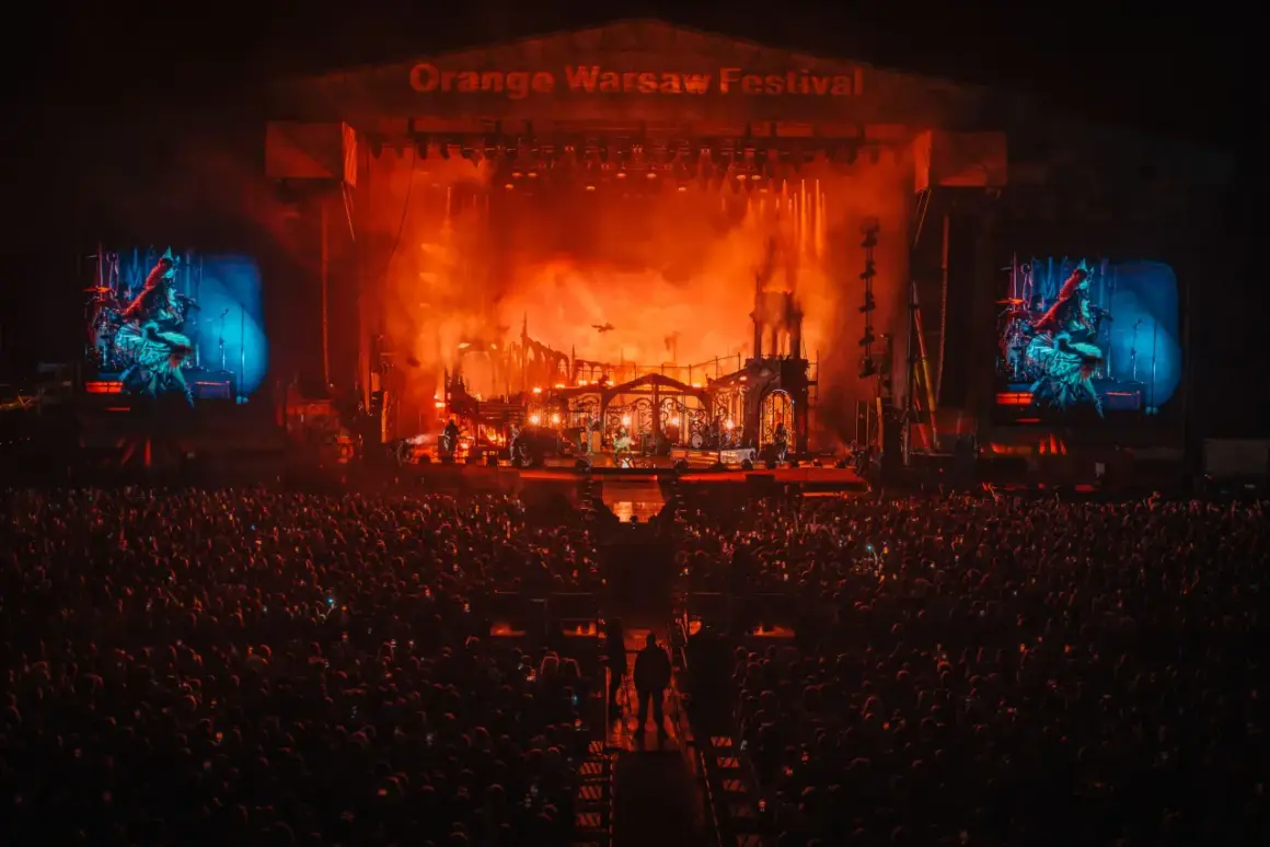 Koncert na Orange Warsaw Festival. Tłum ludzi pod sceną, na której trwa widowiskowe show z efektami pirotechnicznymi.