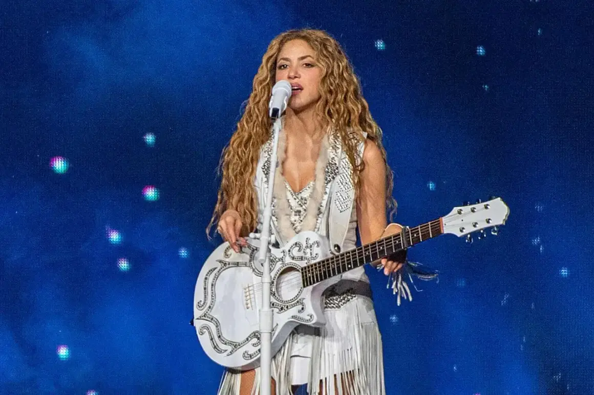 Shakira w Polsce na koncercie, śpiewa z białą gitarą i w białym stroju z frędzlami.