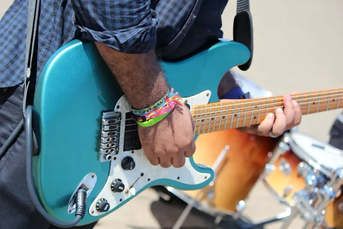 Muzyk grający na turkusowej gitarze elektrycznej, w tle bębny.