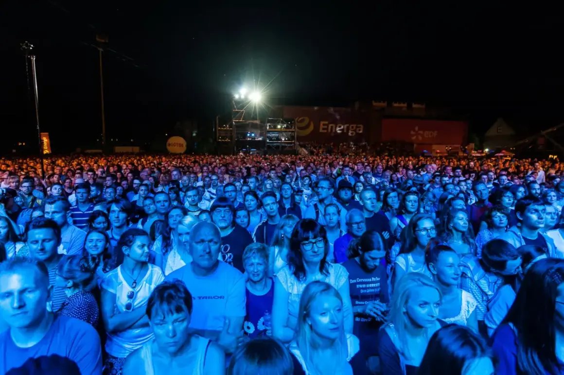 Tłum ludzi na koncercie, oświetlony niebieskim i pomarańczowym światłem. W tle widać banery z logo Energa i Lotos. To prawdziwa inwazja mocy, jak na koncercie Scorpions!