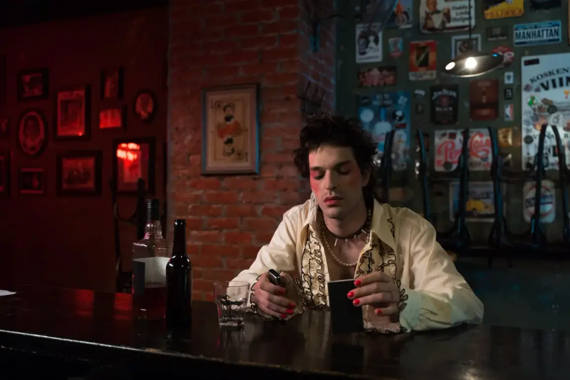 Młoda osoba z makijażem i biżuterią, siedząca przy barze, odzwierciedla ducha punk subkultury.