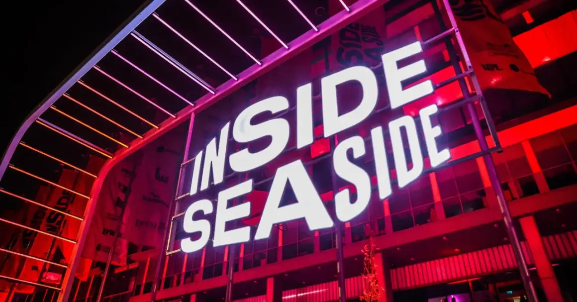 Jasne, oto opis alternatywny:

Duży neon "INSIDE SEASIDE" świeci białym światłem na tle czerwonej, nowoczesnej fasady budynku.