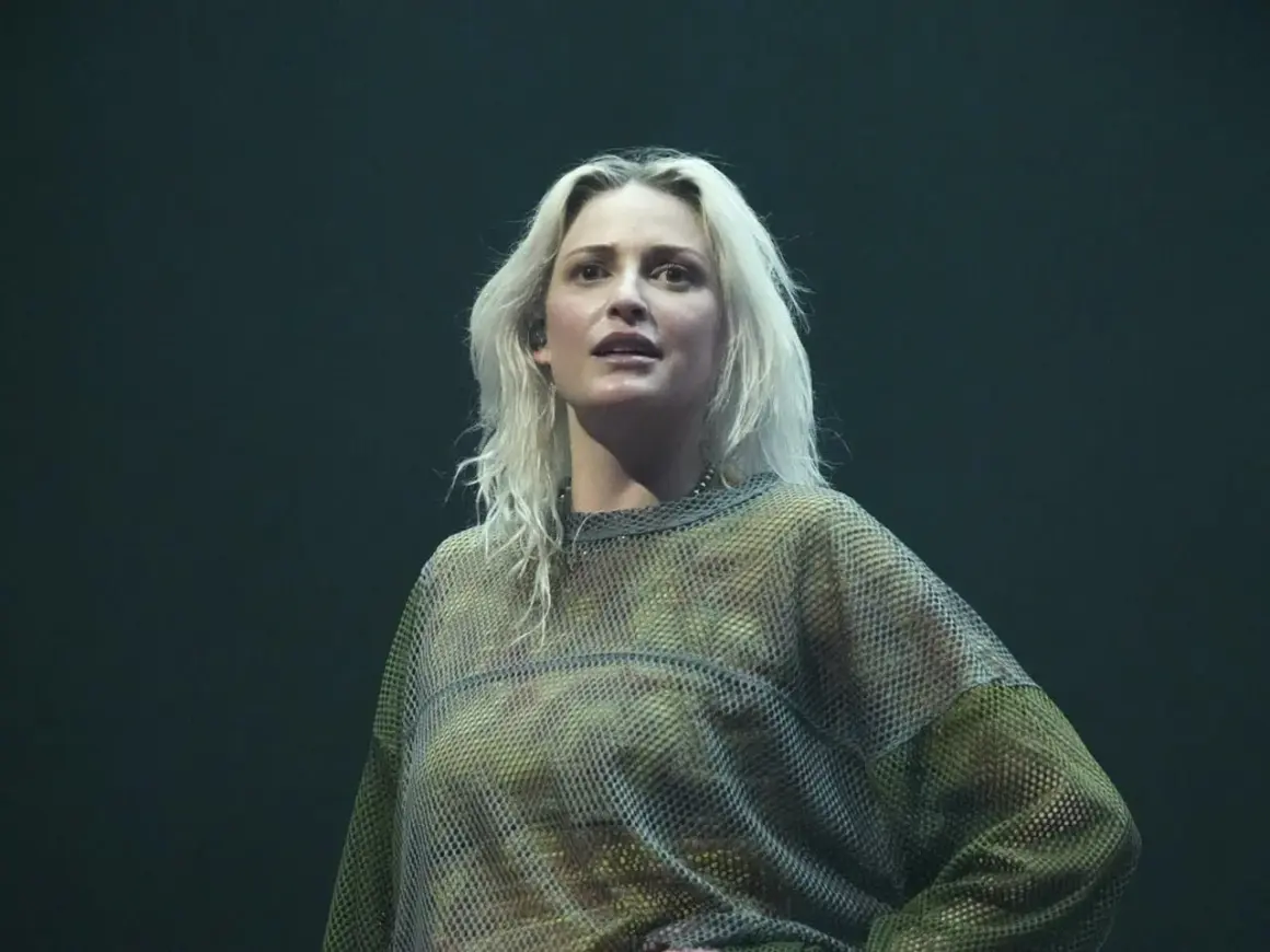 Emily Armstrong w siatkowej bluzce na ciemnym tle.