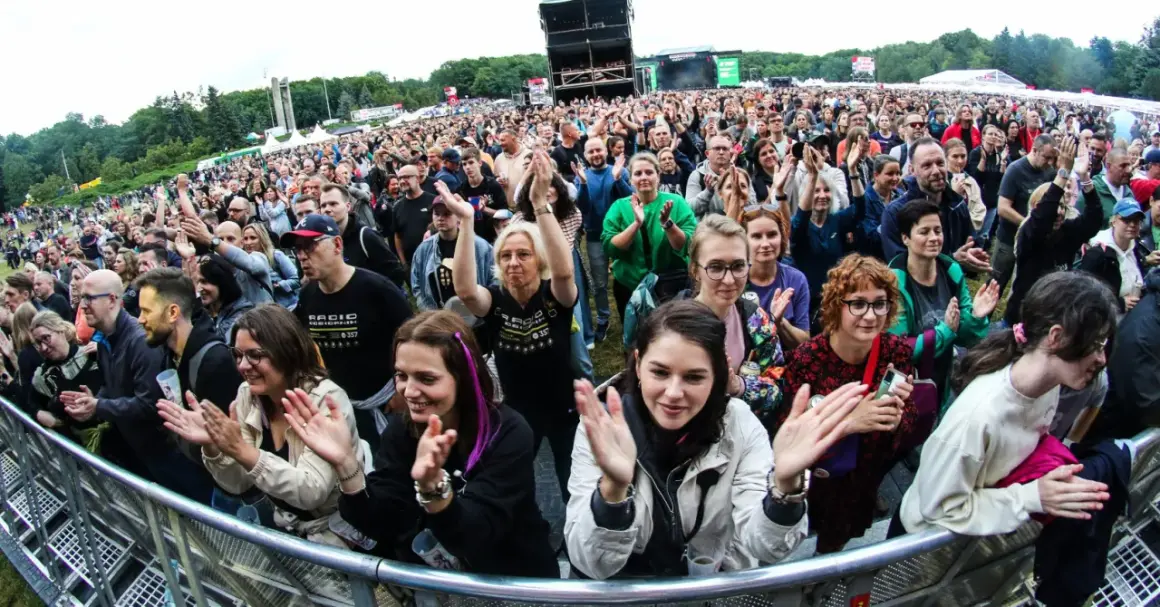 Tłum na koncercie w Poznaniu, fani klaszczą i cieszą się występem. Widoczny fragment sceny i festiwalowej atmosfery.