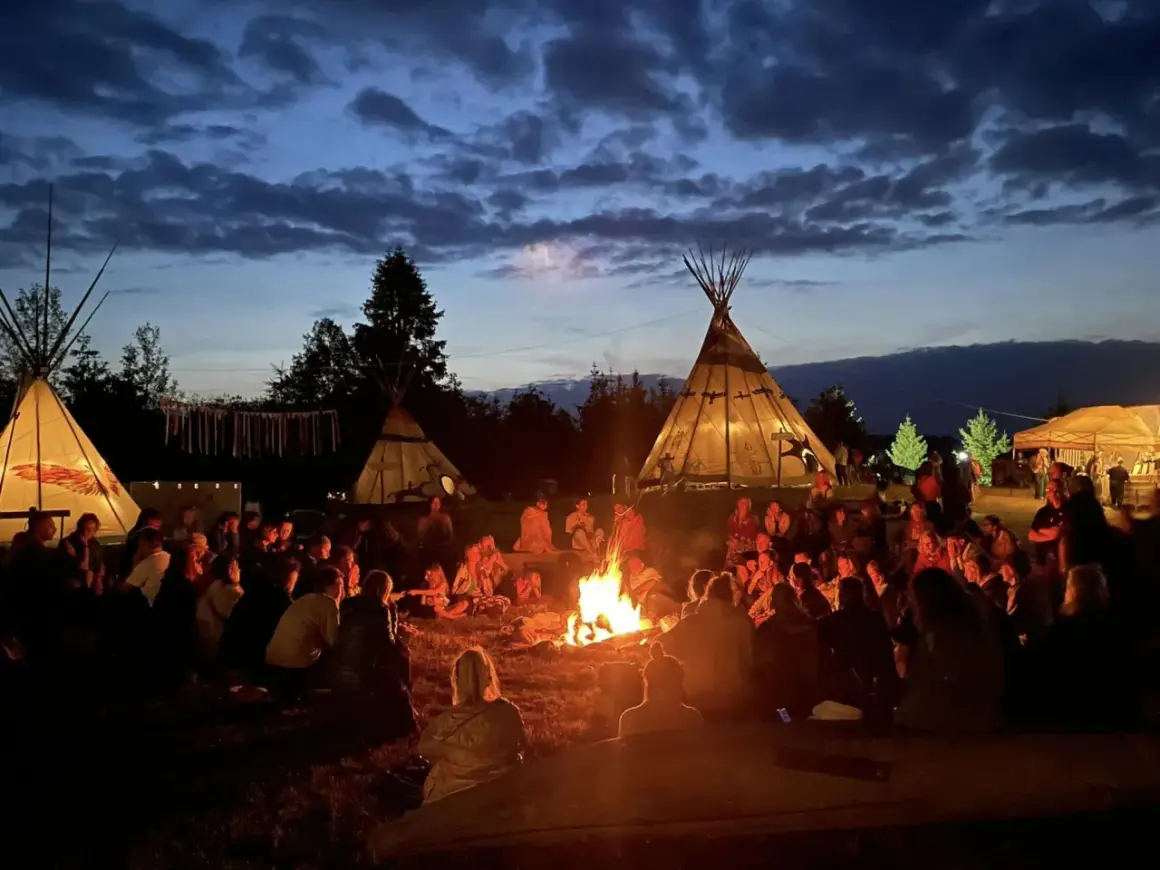 Ludzie siedzą przy ognisku pod namiotami tipi, tworząc atmosferę jednego z wielu festiwali na świecie.