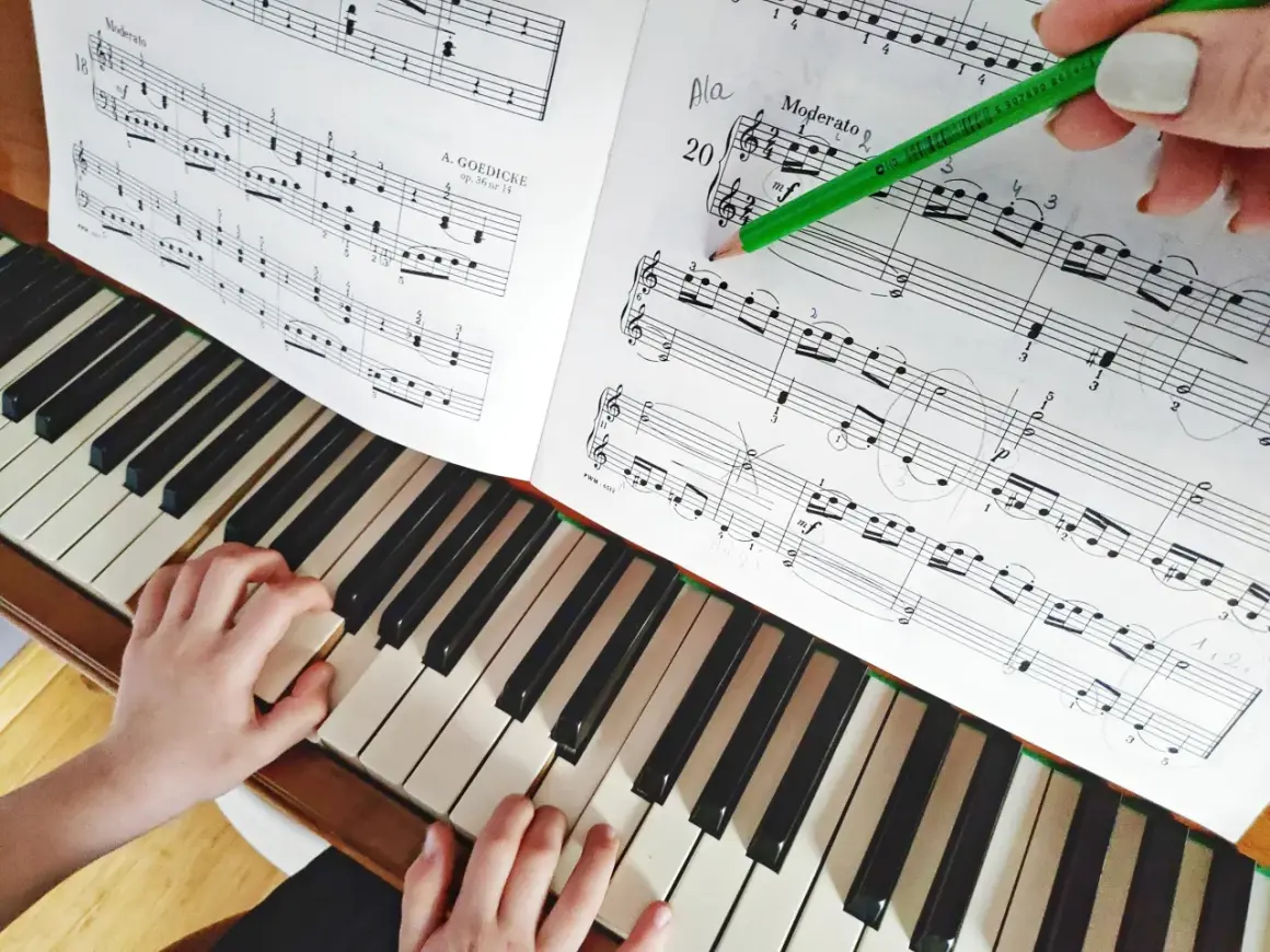 Dziecko uczy się gry na keyboardzie, ćwicząc nuty z podręcznika. Zielony ołówek zaznacza fragment do nauki.