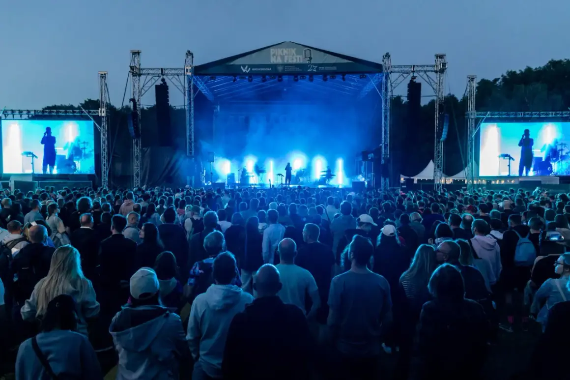 Koncert na festiwalu w Cytadeli, tłum ludzi przed sceną oświetloną niebieskim światłem.